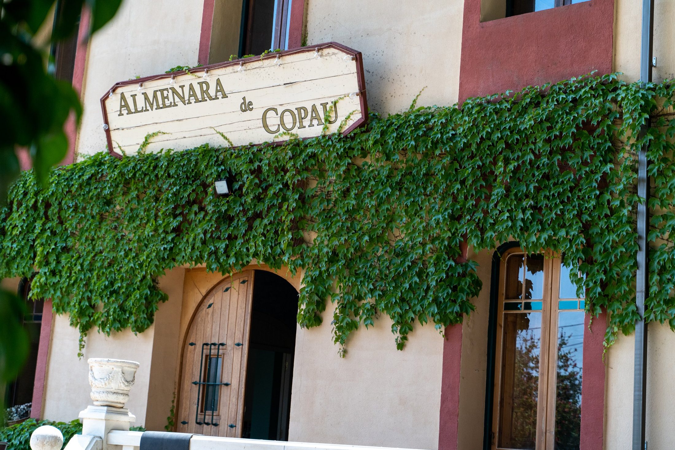 Fachada de la finca con el cartel entre la hiedra